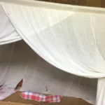 Cama doble con mosquitera colgada del techo y remetida bajo el colchón